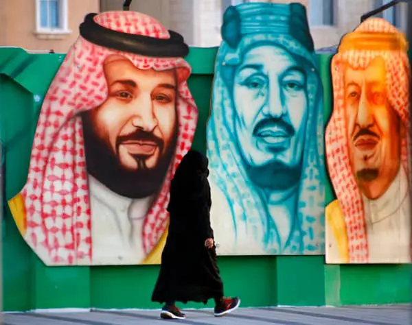 امرأة تسير أمام لافتة في الدمام تظهر العاهل السعودي الملك سلمان، إلى اليمين، ولي عهد محمد بن سلمان، إلى اليسار، ومؤسس المملكة العربية السعودية الراحل الملك عبد العزيز آل سعود الائتمان: ا ف ب الصور / عمرو نبيل