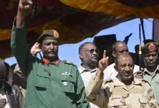 أمير الجهاديين الشيخ عبد الرحمن محمد موسى، المنسق العام للدفاع الشعبى رافعاً السبابة مهللاً و مكبراً، يشرّف إحدى فعاليات الدفاع الشعبى، وبجانبه عبد الفتاح البرهان