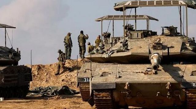 جنود إسرائيليون يتجمعون بالقرب من الدبابات بينما يتصاعد الدخان من غزة في الخلفية، بعد انتهاء وقف إطلاق النار
