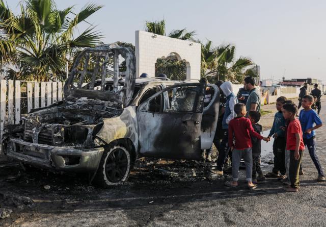 أشخاص يقفون بالقرب من سيارة مدمرة تابعة لمنظمة المطبخ المركزي العالمي