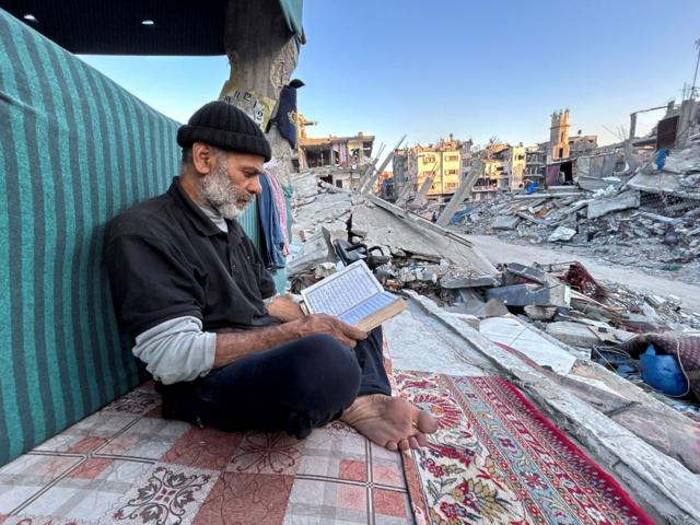رجل فلسطيني يقرأ القرآن وهو ينتظر الإفطار بينما يجلس على أنقاض منزله المدمر شمال قطاع غزة