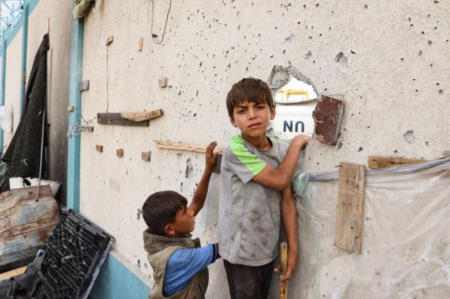 طفلان فلسطينيان يقفان بالقرب من مبنى متضرر في موقع غارة إسرائيلية على مخيم للنازحين في رفح، في 28 مايو/أيار 2024
