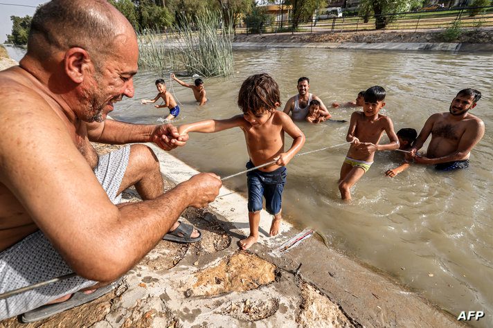 A boy uses a rope to come out of the water from a canal of the Tigris river in Baghdad amid a soaring heatwave on June 18, 2024…