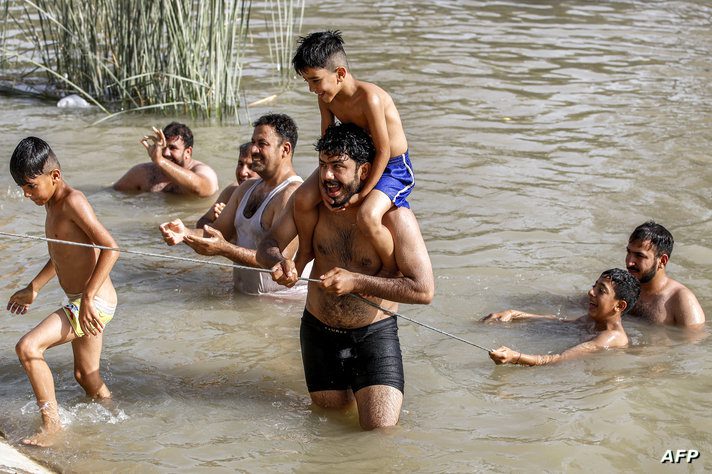 A man carrying a child on his shoulders uses a rope to come out of the water from a canal of the Tigris river in Baghdad amid a…
