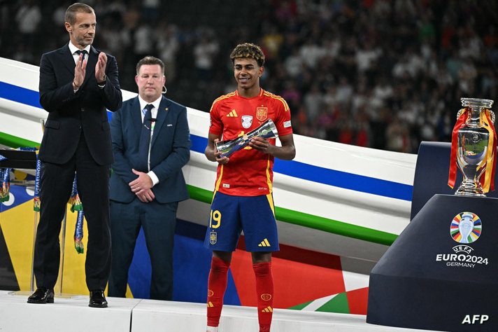 Spain's forward #19 Lamine Yamal (C) celebrates with the Best Young player trophy next to UEFA President Aleksander Ceferin (L)…